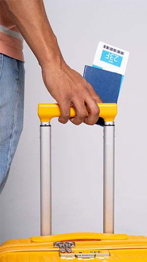 A person holds the handle of a yellow suitcase, with a passport and boarding pass in hand. The mood suggests anticipation for travel or a journey.